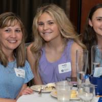 Three alumni smile together at their table